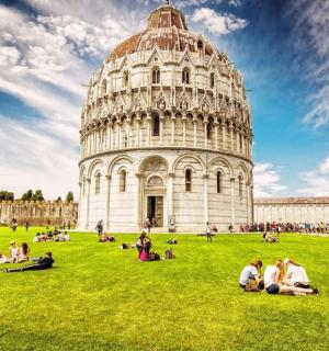 skupina lidí sedících v trávě před šikmou věží