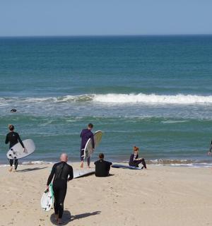 Skupina lidí kráčejících po pláži se surfovými prkny
