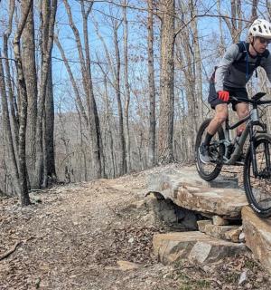 a man riding a bike over a rock in the woods