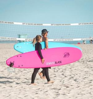 two people walking on the beach with their surfboards