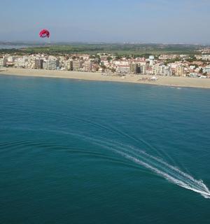 a boat in the water with a kite flying over a beach