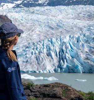 一位女士站在山顶上,看着冰川