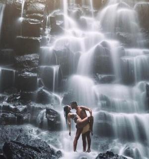 a man and a woman standing in front of a waterfall