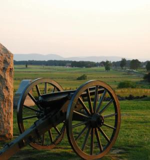 a cannon in a field with a statue in the background