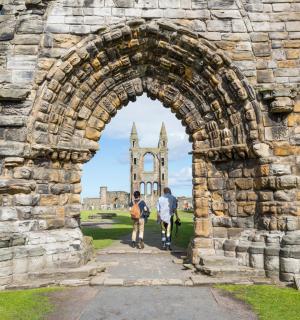 两个人走过一座石拱门,背景是一座教堂