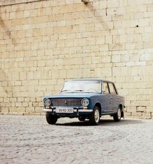 一辆蓝色的旧车停在砖墙旁边