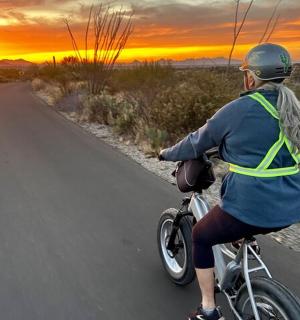 žena jedoucí na kole po silnici při západu slunce
