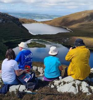 skupina lidí sedících na skále s výhledem na jezero