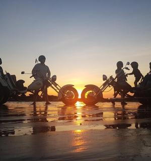 日落时分，一群人在海滩上骑着摩托车