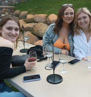 tři ženy sedící u stolu s vinnými sklenicemi