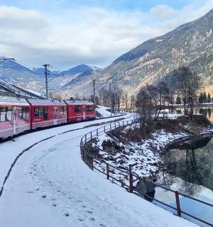a red train on a snowy track next to a river
