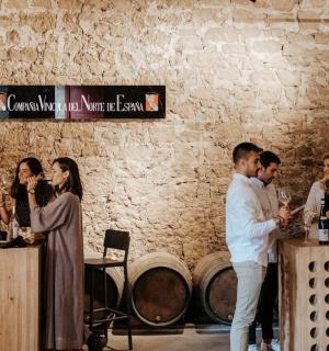 skupina lidí stojících u stolů s lahvemi vína