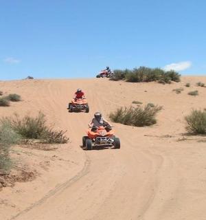 three people riding atvs on a dirt road in the desert