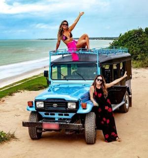 two women sitting on top of a jeep on the beach