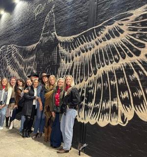a group of people standing in front of a large bird mural