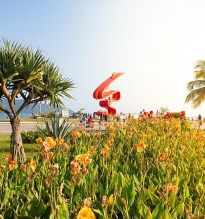 a sculpture in a park with flowers and palm trees