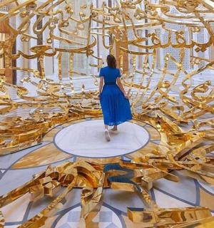 a woman in a blue dress walking in a gold room