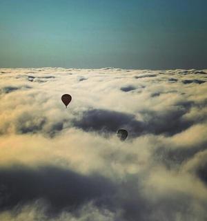 two hot air balloons flying above the clouds