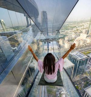 a woman is sitting on the glass floor of a skyscraper