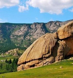 a large rock on a hill with mountains in the background