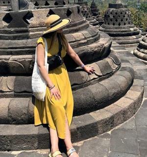 a woman wearing a yellow dress and a hat standing next to a fountain