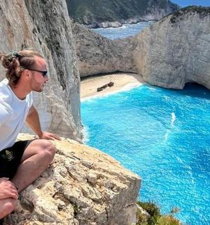 一名男子坐在海滩边的一块岩石上