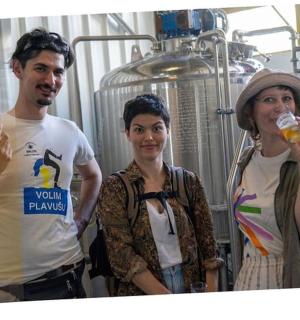 three people standing in a brewery with a man drinking from a glass