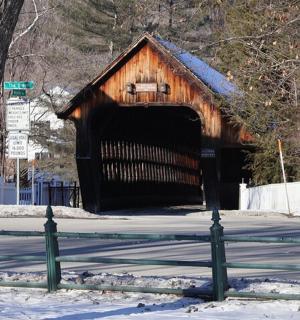 a wooden covered bridge in the snow with a fence