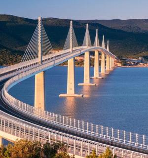 μια γέφυρα πάνω από ένα υδάτινο σώμα με βουνά στο φόντο