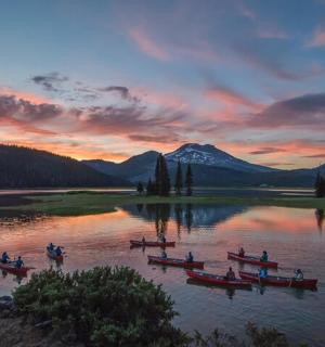 eine Gruppe von Menschen in Booten auf einem See bei Sonnenuntergang