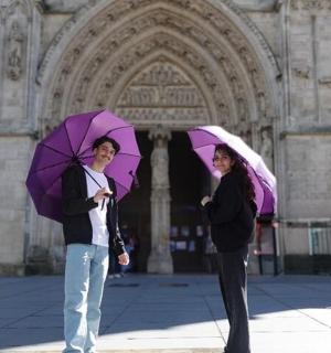 两个人站在一栋建筑前，手里拿着紫色的雨伞