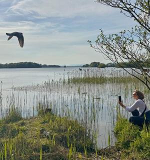 una donna che scatta una foto di un uccello che vola sopra un lago