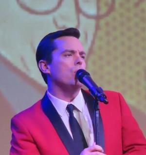 一名身穿红色西装的男子对着麦克风讲话