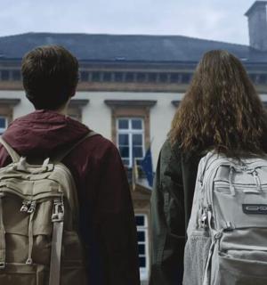 zwei Personen mit Rucksäcken stehen vor einem Gebäude