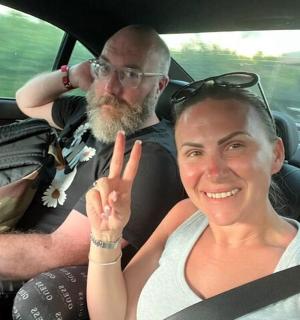 muž a žena sedící v autě a dávají znamení míru