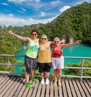 three women standing on a bridge over a blue lake