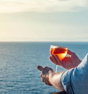 osoba držící drink před oceánem