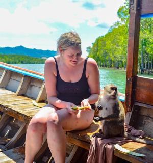 一名女子坐在码头上，带着一只正在吃食物的狗
