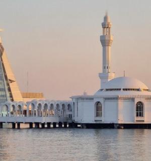 a white mosque on the water with a tall building