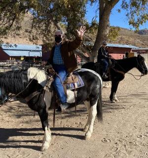 a man waving while riding a horse on a dirt road