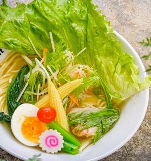 a bowl of soup with lettuce and vegetables on a table