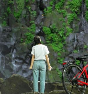一位女士站在瀑布旁边，骑着自行车