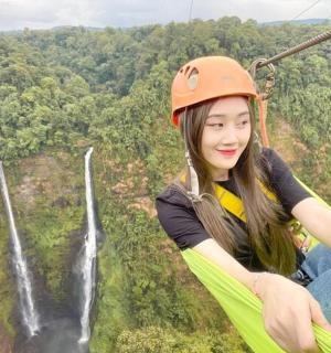 a woman riding on a zip line in front of a waterfall