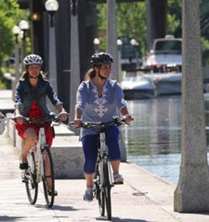 three women riding bikes down a sidewalk next to a river
