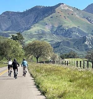 two people riding bikes down a road with mountains in the background