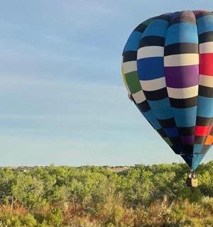 Barevný horkovzdušný balón letící nad polem