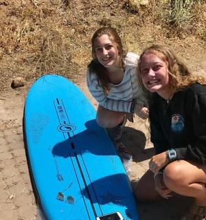 two women are kneeling next to a blue surfboard