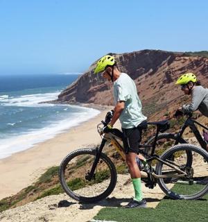 two people with bikes on a hill near the beach