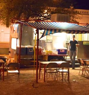 muž stojící před pojízdným stánkem s jídlem a stoly a židlemi