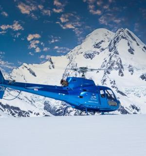 一架蓝色直升机停在一座白雪皑皑的山前